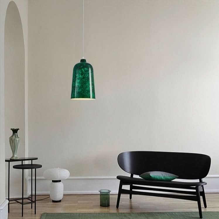 Ambiance intérieure avec suspension verte, banc noir, vases et tapis vert.