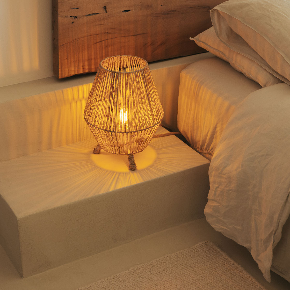 Lampe allumée posée sur une marche de chevet, près d'un lit en lin beige.
