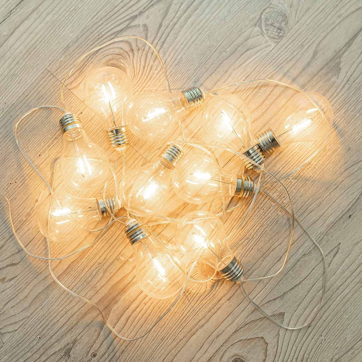 Guirlande posée sur un parquet en bois clair, ampoules transparentes regroupées et allumées
