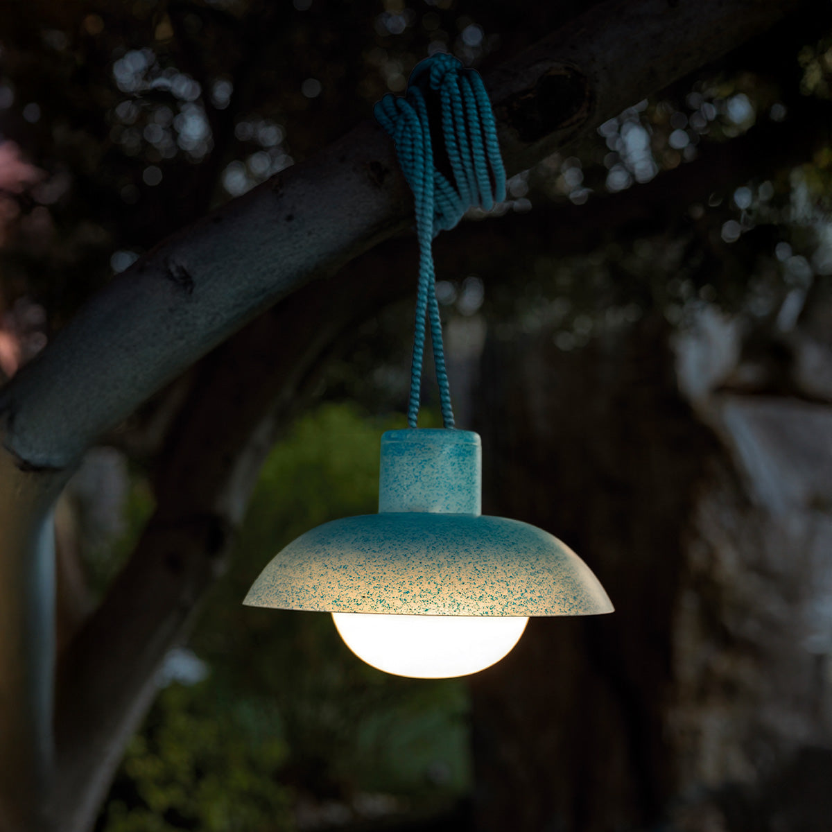 Suspension bleu canard patinée suspendue par un cordon tressé, branche et jardin au crépuscule