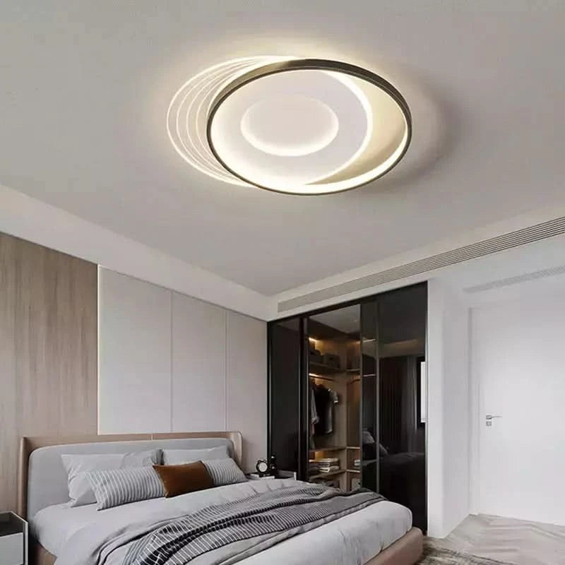 Plafonnier rond cerclé de noir, éclairé au-dessus d'un lit gris