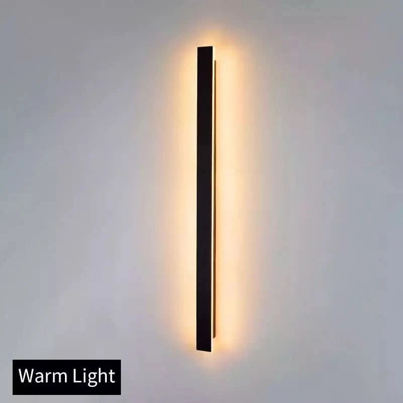 Même applique murale noire en lumière chaude, halo doré projeté sur un mur neutre.