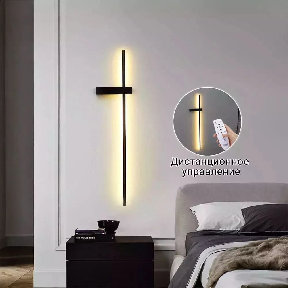 Applique noire en forme de croix sur mur blanc, halo lumineux chaud, télécommande en médaillon