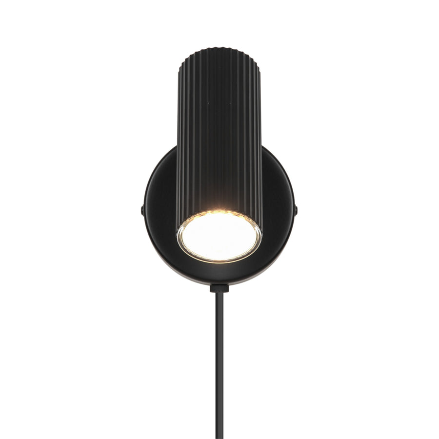 Vue frontale de l’applique noire, tête cylindrique cannelée éclairée vers le bas.