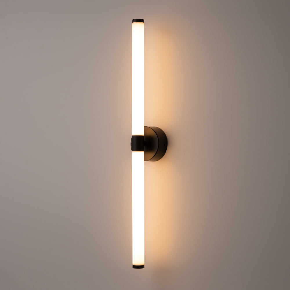 Applique verticale allumée diffusant une lumière chaude sur un mur beige clair