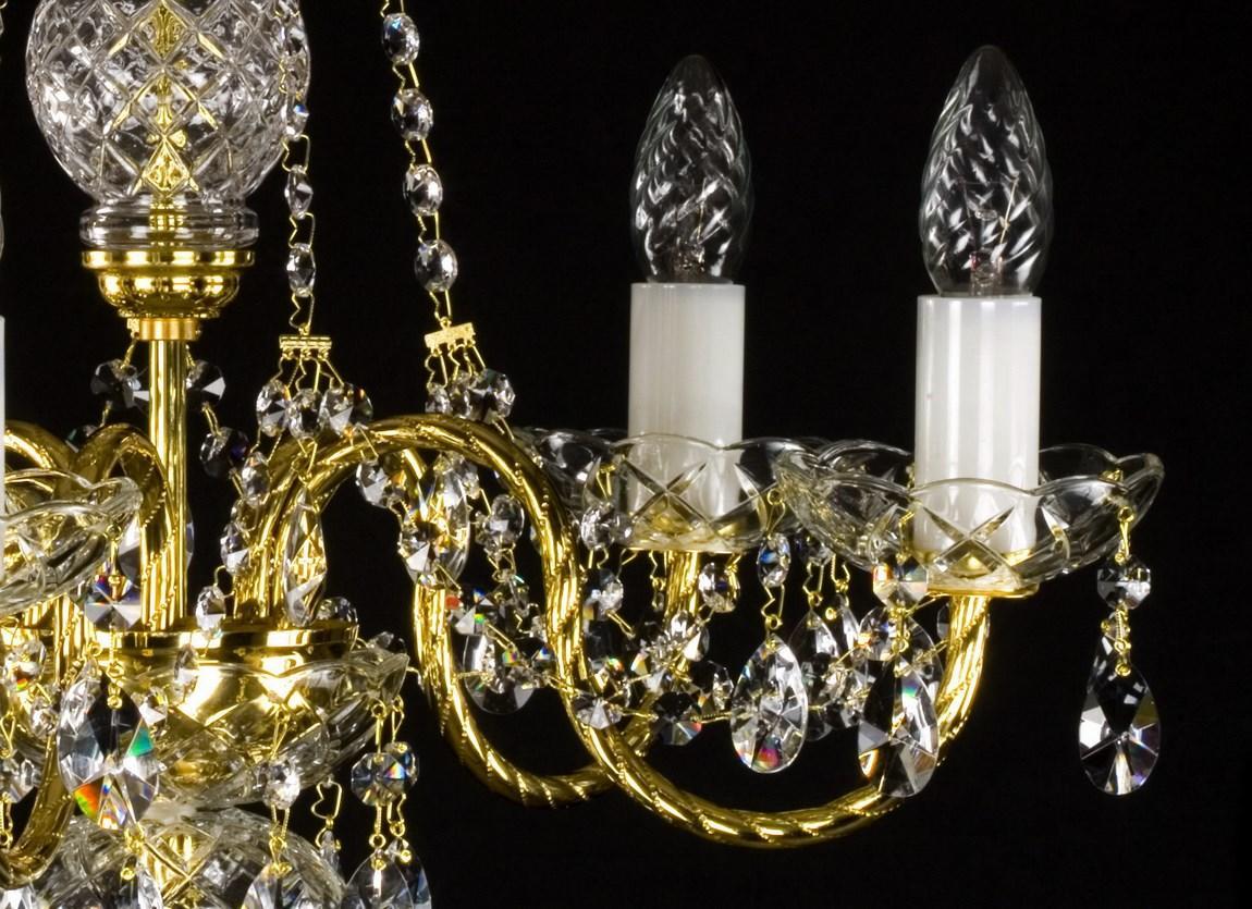Gros plan sur deux bras du lustre, coupelles et pendeloques en cristal.