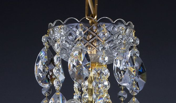 Vue rapprochée du sommet, chaîne dorée et couronne de cristaux du luminaire.