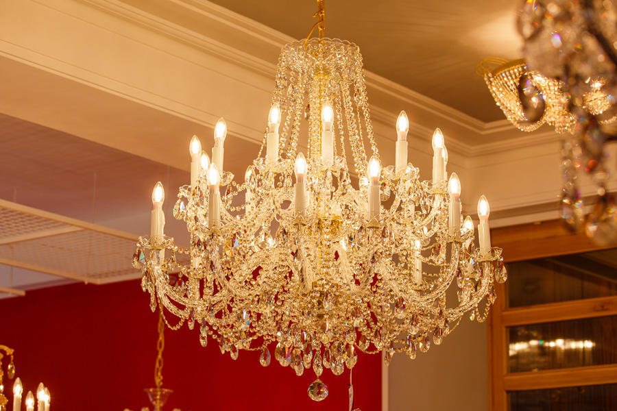 Gros plan du lustre illuminé en magasin, fond rouge, cristaux et chaînettes bien visibles.