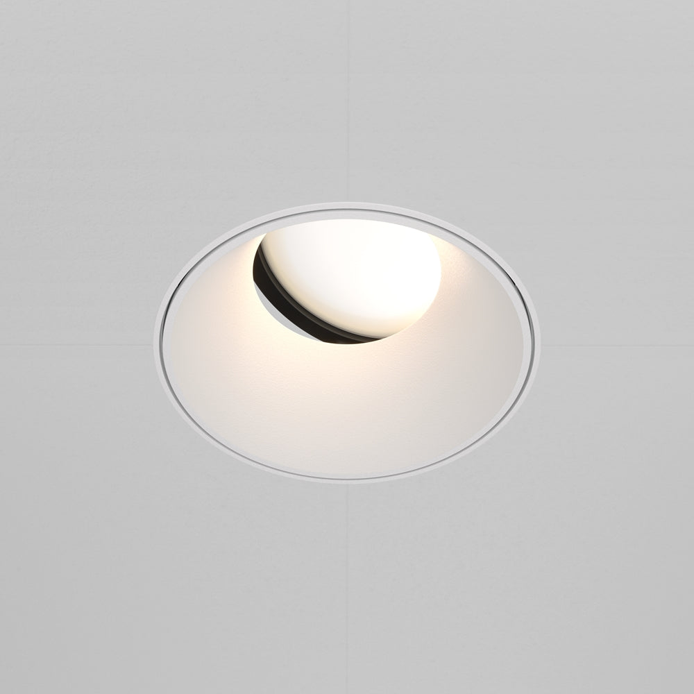 Spot encastré rond au plafond, halo lumineux blanc et bordure fine.