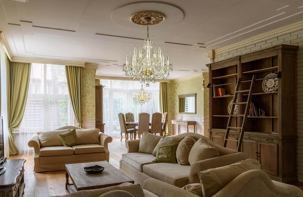 Lustre suspendu au plafond d'un salon classique, canapés beiges et bibliothèque en bois