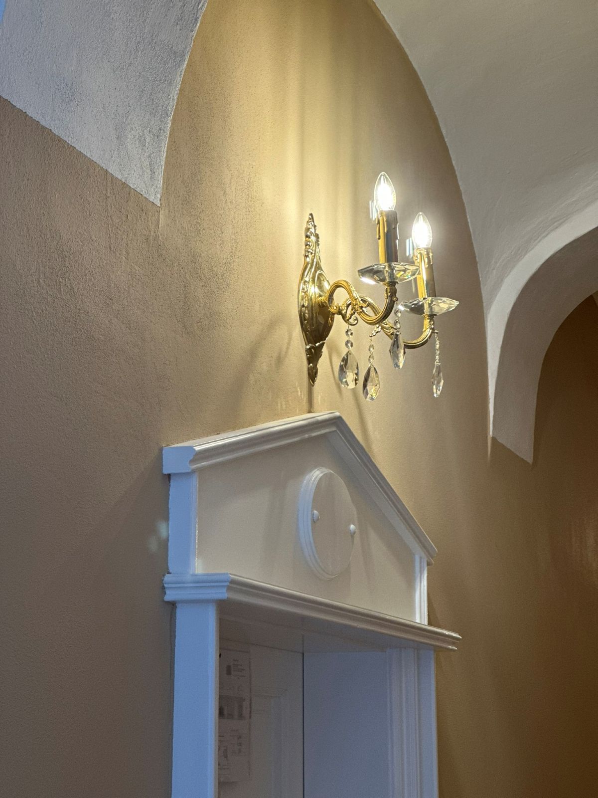 Vue en biais de l'applique dorée éclairée, installée au-dessus d'une porte blanche