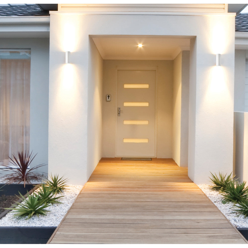 Deux appliques murales blanches éclairent une entrée extérieure moderne avec porte et jardinières.
