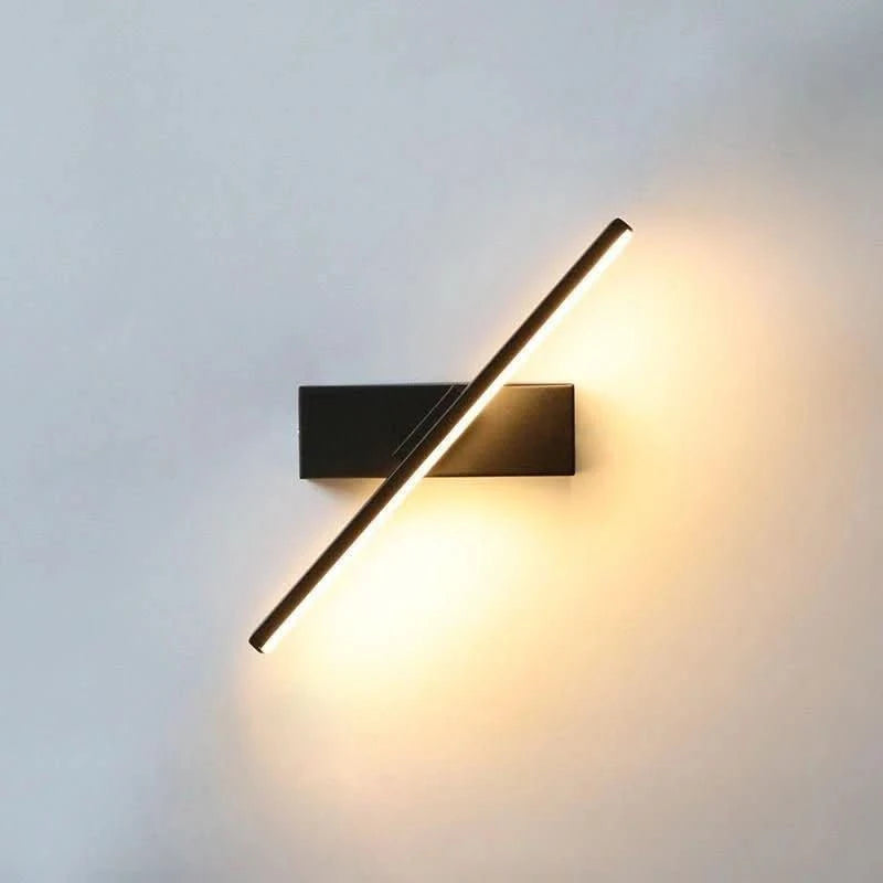 Applique noire allumée sur mur clair, halo lumineux diffusé vers le haut et le bas