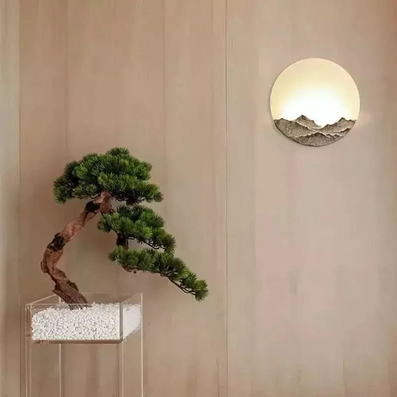 Luminaire mural rond installé sur paroi boisée près d'un bonsaï pin en pot