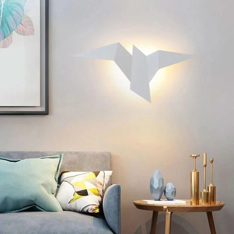 Applique murale blanche en forme d'oiseau origami, allumée au-dessus d'un canapé avec coussins.