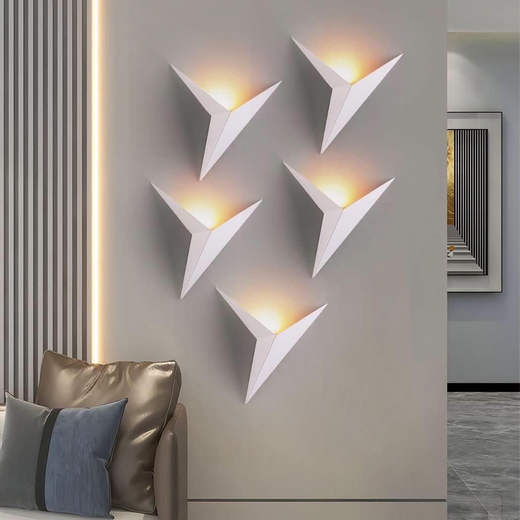Cinq appliques murales blanches en forme d'étoile pliée, éclairées sur un mur beige
