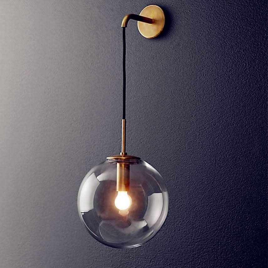 Version laiton doré du luminaire mural, bras coudé et globe de verre clair.