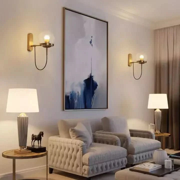 Deux appliques dorées éclairant un mur blanc au-dessus d'un canapé beige encadré