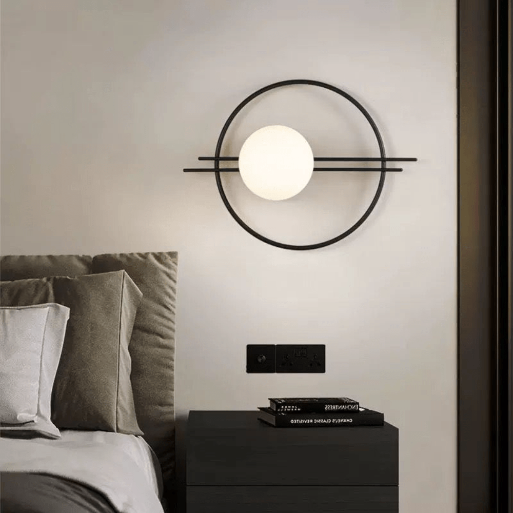 Version noire du luminaire mural fixée sur un mur beige près d'une table de nuit