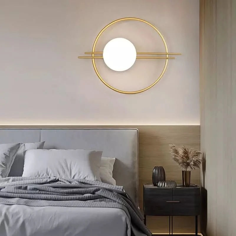 Applique murale dorée ronde installée au-dessus d'une tête de lit grise en ambiance chambre