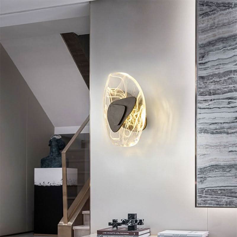 Applique murale dorée installée dans un escalier, éclairant un mur avec une œuvre en marbre.