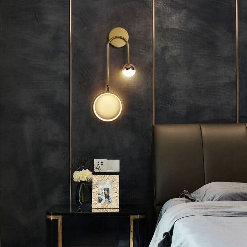 Applique murale dorée sur fond sombre, cercle lumineux et sphère éclairée.