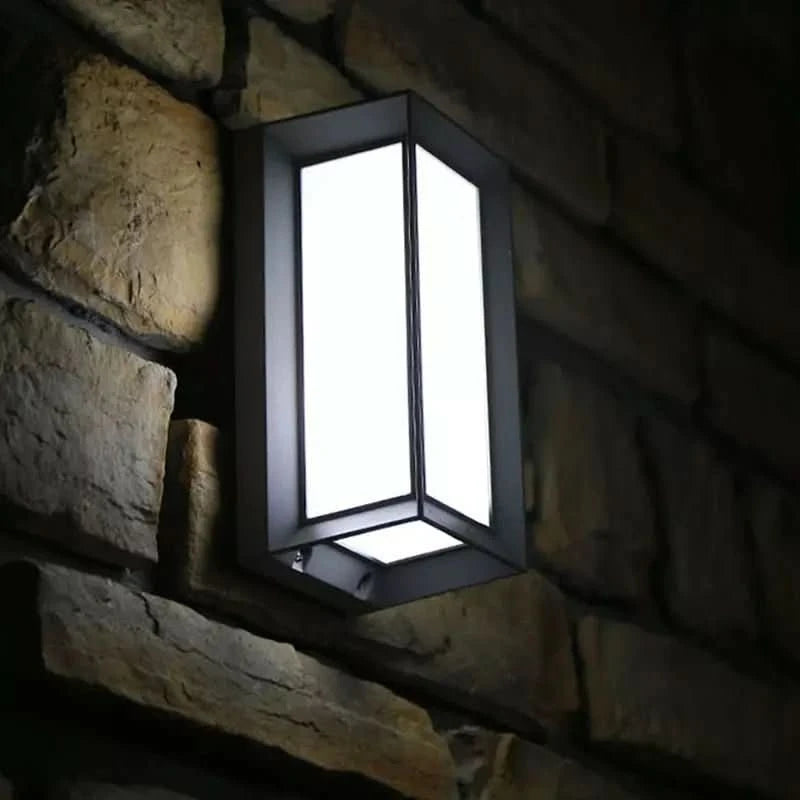 Gros plan du luminaire éclairé sur mur en pierre, cadre noir et diffuseur blanc.