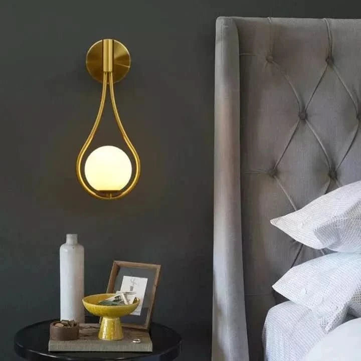 Applique dorée allumée contre un mur anthracite, tête de lit capitonnée en velours gris