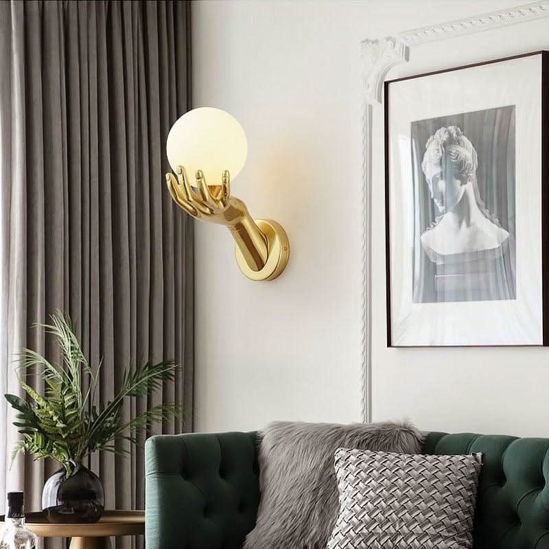 Mise en ambiance salon : applique murale dorée au-dessus d'un canapé vert et d'un cadre.