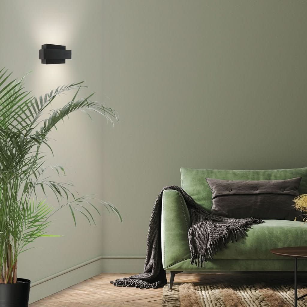 Applique murale noire fixée sur un mur vert au-dessus d'un canapé et d'une plante.