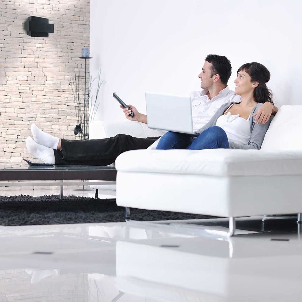 Mise en ambiance avec un couple sur canapé blanc, applique murale noire au mur en pierre.
