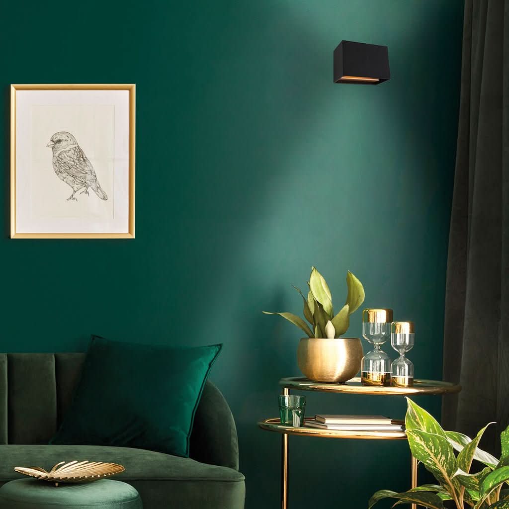 Mise en ambiance sur mur vert bouteille, applique noire diffusant une lumière chaude vers le bas.