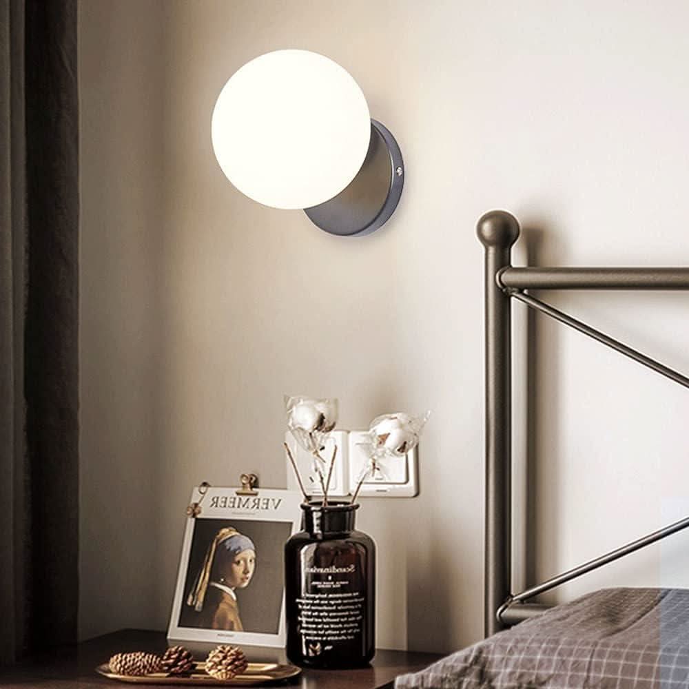 Applique noire allumée près d'un lit, cadre photo et vase en verre sombre