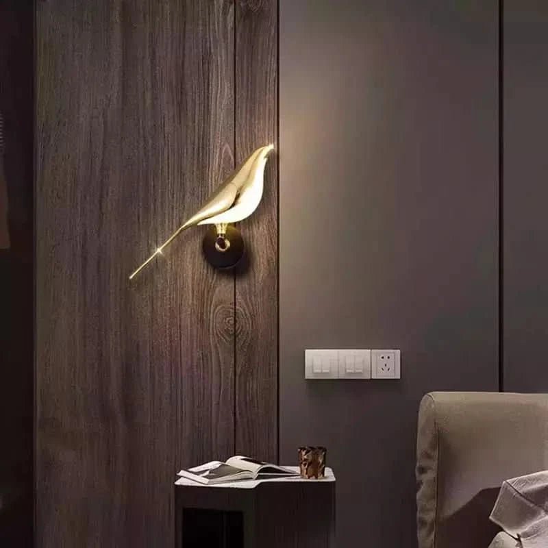 Vue de face d'une applique oiseau doré allumée sur lambris bois foncé.