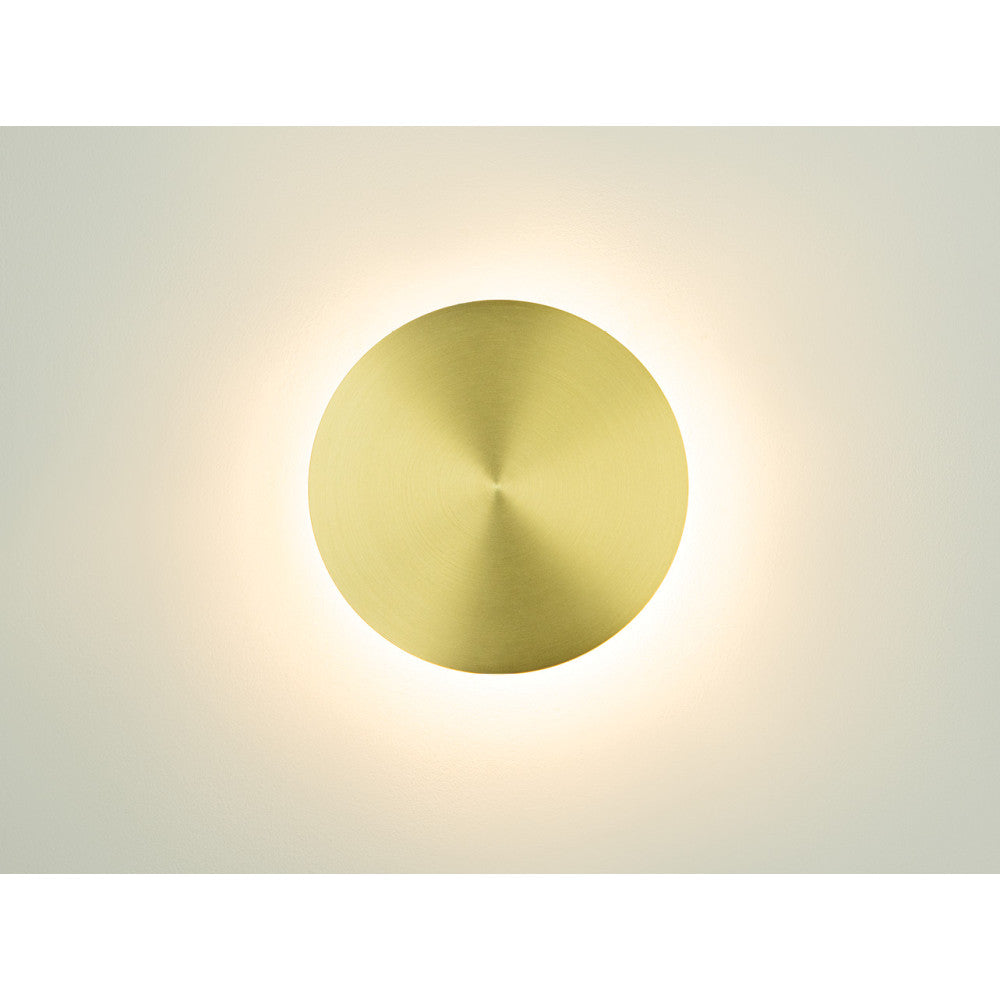 Applique ronde en laiton allumée projetant un halo lumineux diffus sur le mur