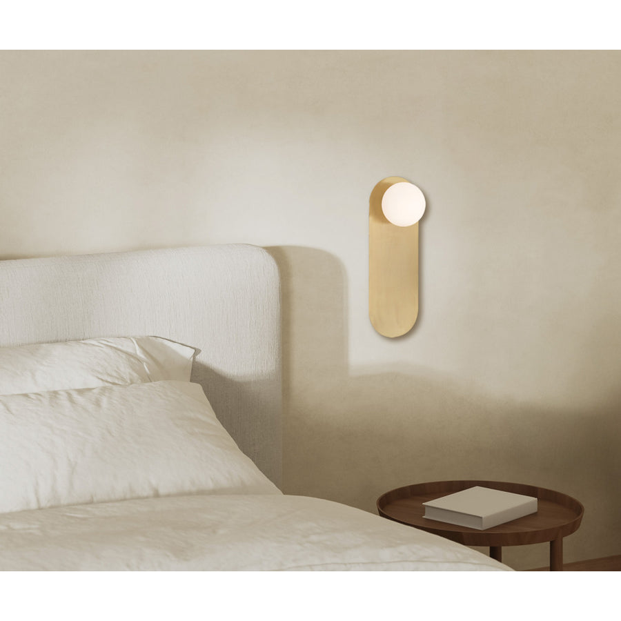 Applique dorée allumée au-dessus d’une tête de lit blanche avec table de chevet.