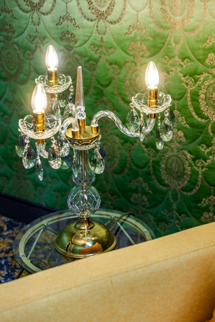 Mise en ambiance sur table verre, papier peint vert, lampe allumée près d'un fauteuil.