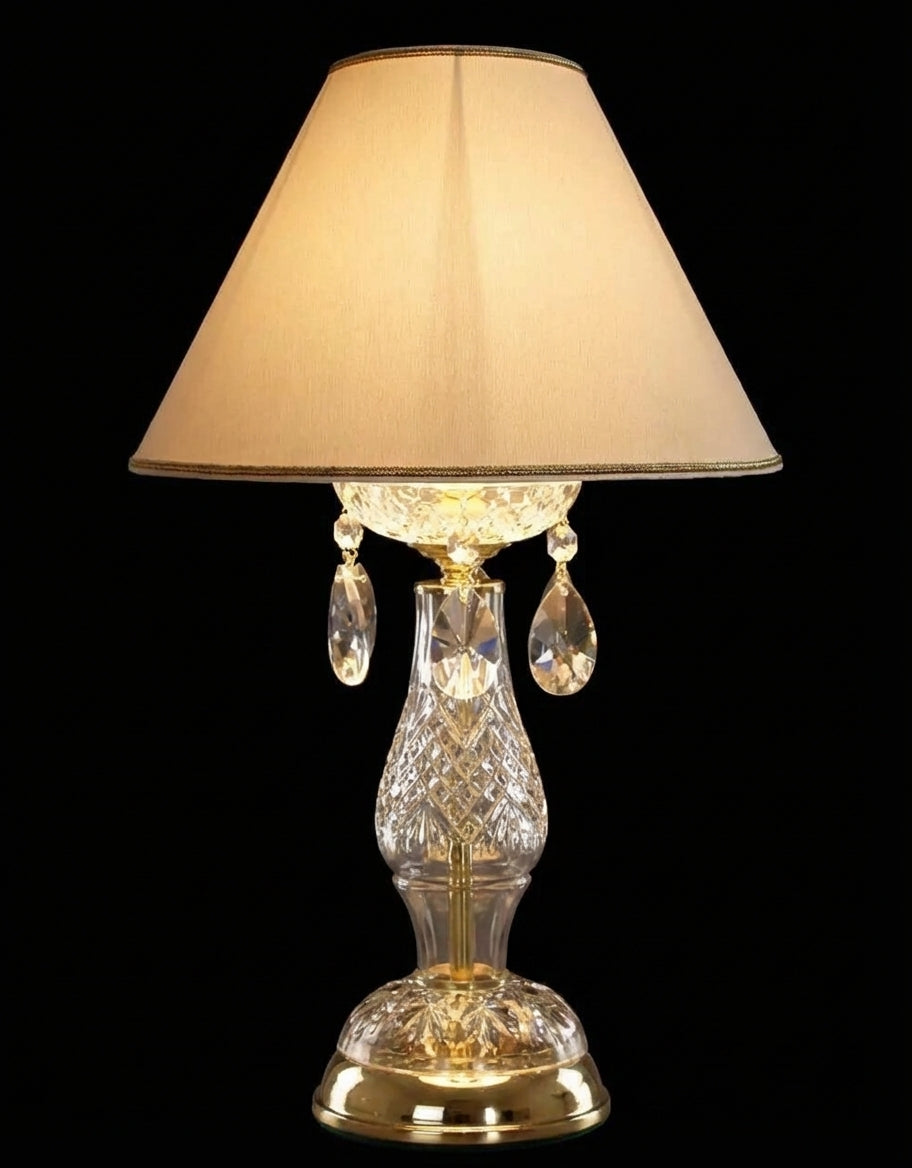 Détail de la finition dorée et du cristal taillé, lampe allumée sur fond noir.