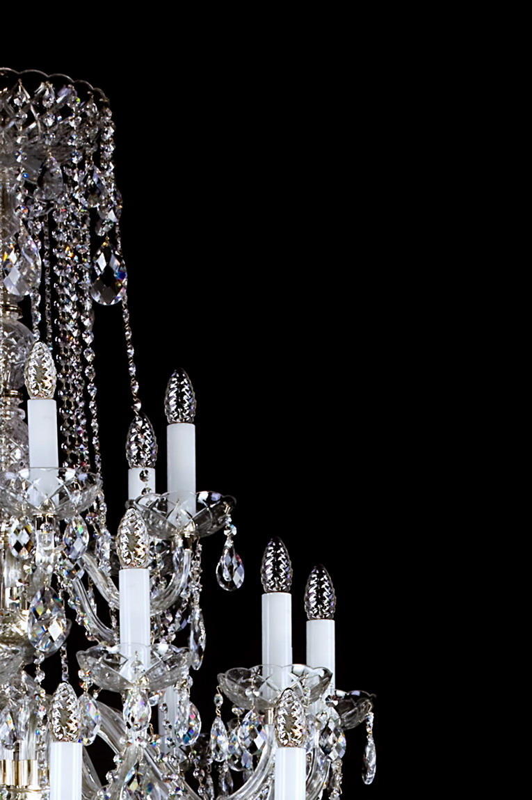 Détail des bras courbes, bougies blanches et grappes de cristal du luminaire.