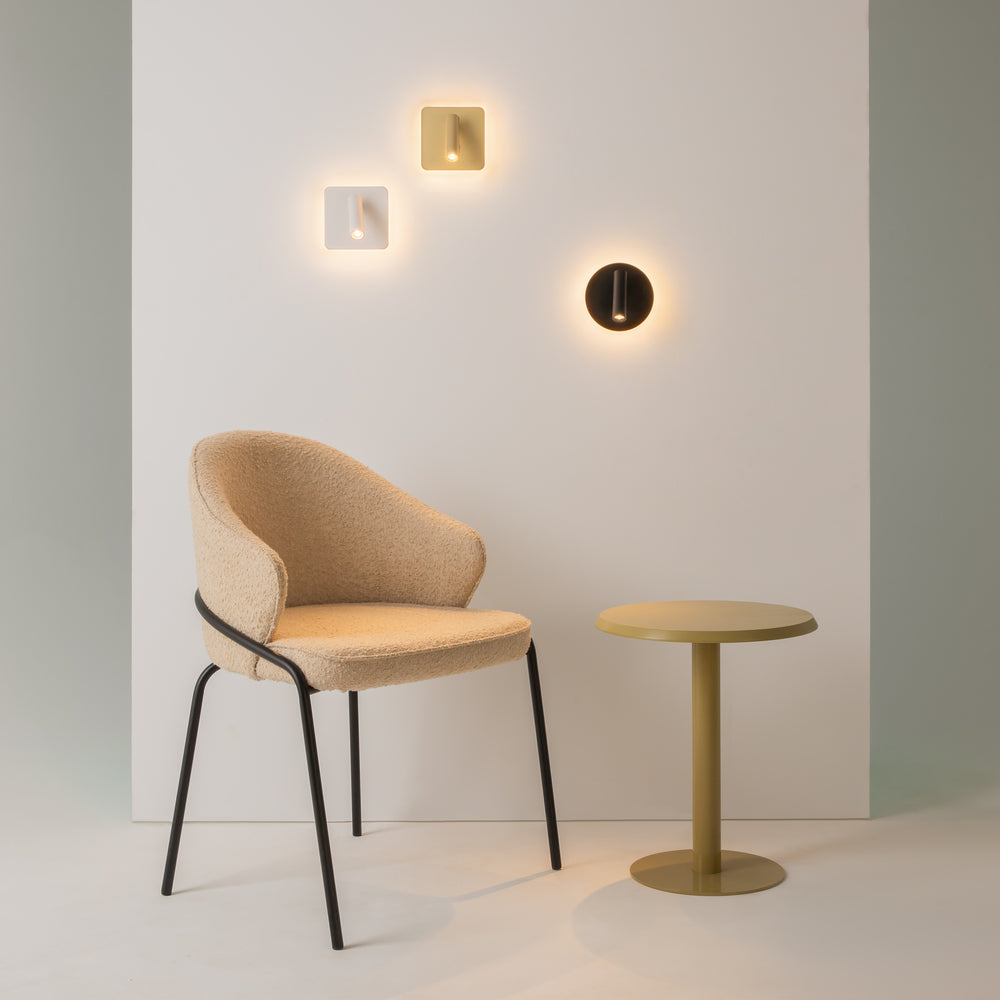Mise en ambiance de trois appliques murales éclairées au-dessus d'un fauteuil beige.