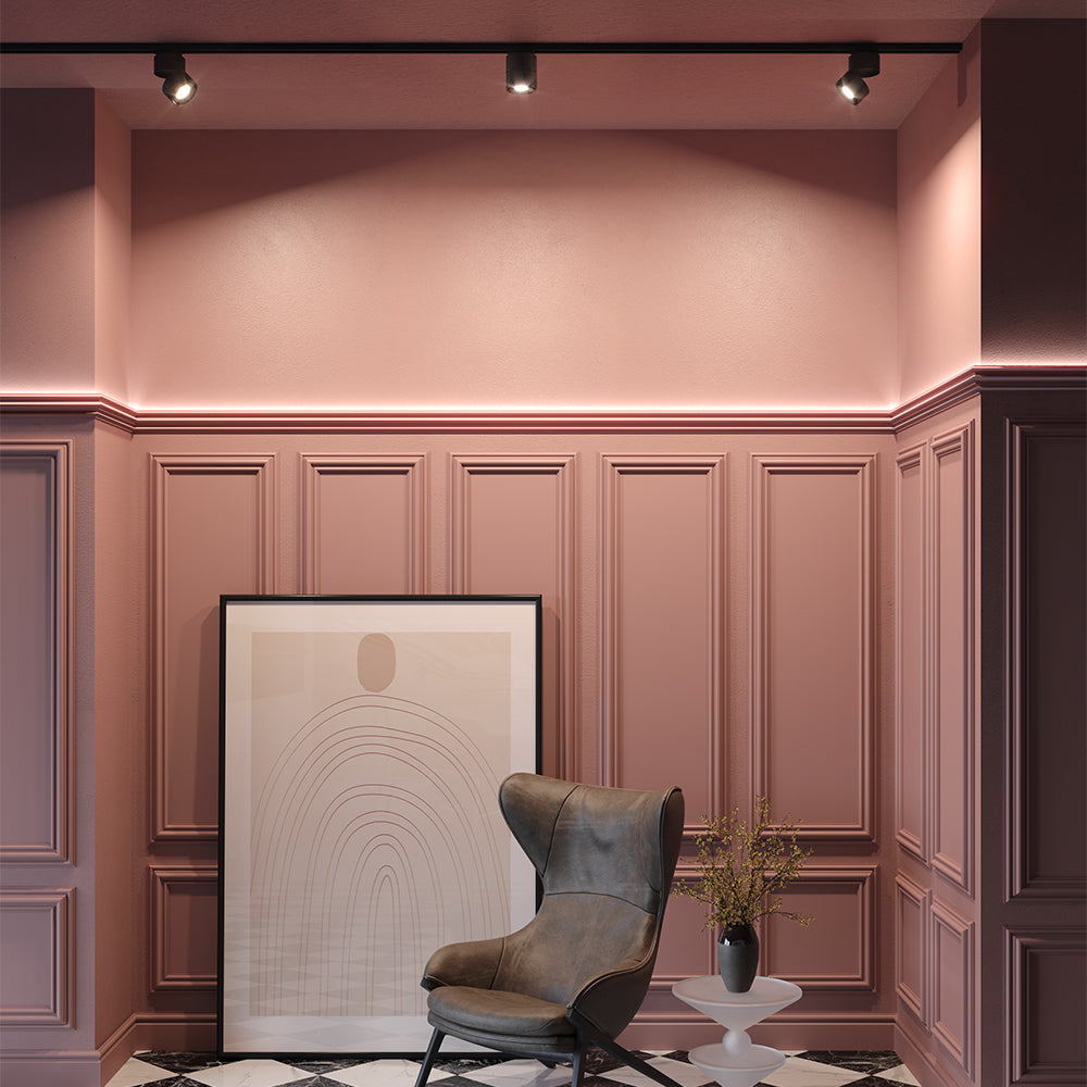 Trois spots noirs sur rail éclairant un intérieur rose avec fauteuil et tableau.