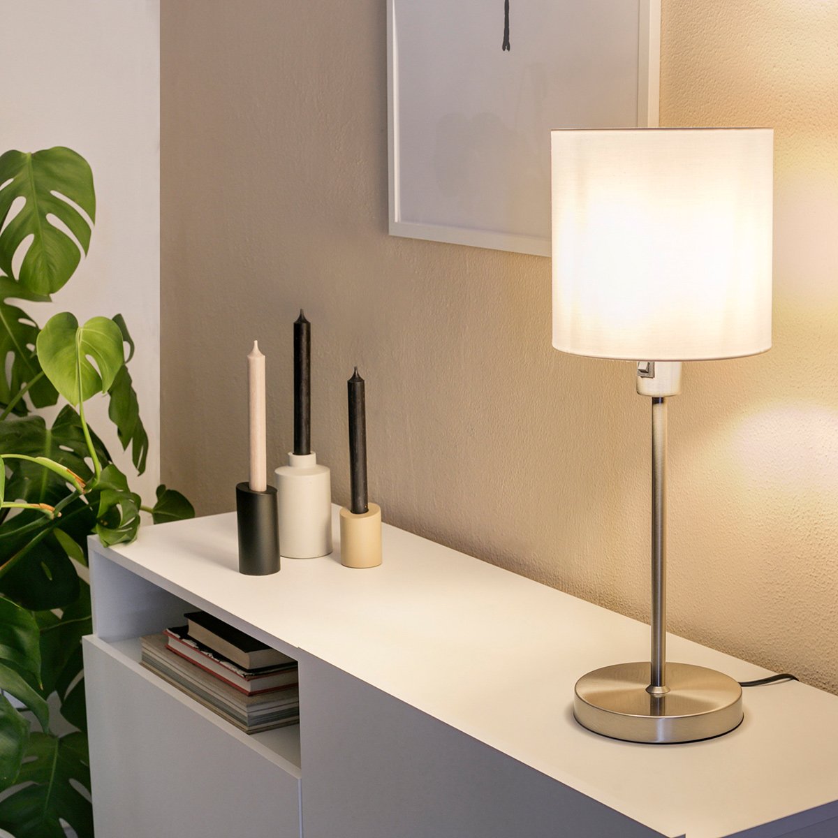 Mise en ambiance sur un meuble blanc, lampe allumée près de bougies