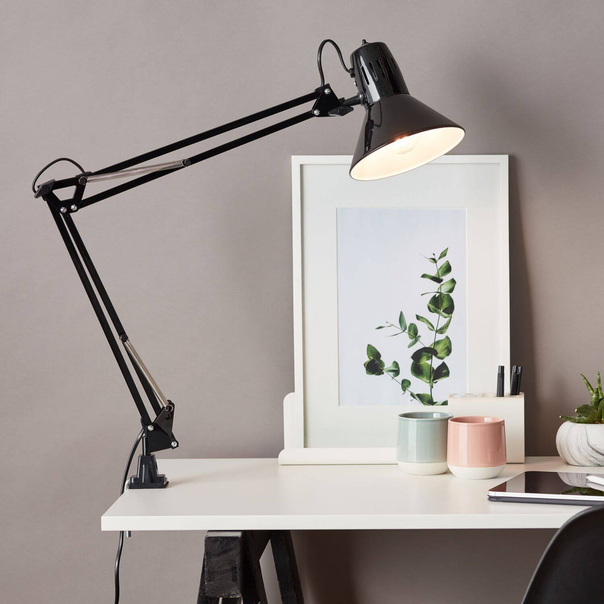 Mise en ambiance du bureau éclairé, lampe allumée au-dessus d'un cadre et deux tasses