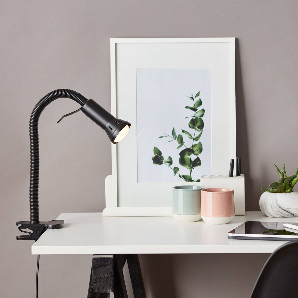 Ambiance bureau : lampe noire à pince éclairant un plan de travail avec cadre, tasses et tablette.