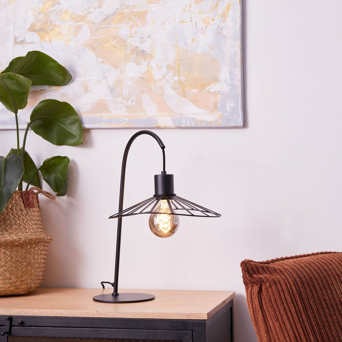 Lampe allumée dans un intérieur avec plante verte et coussin terracotta