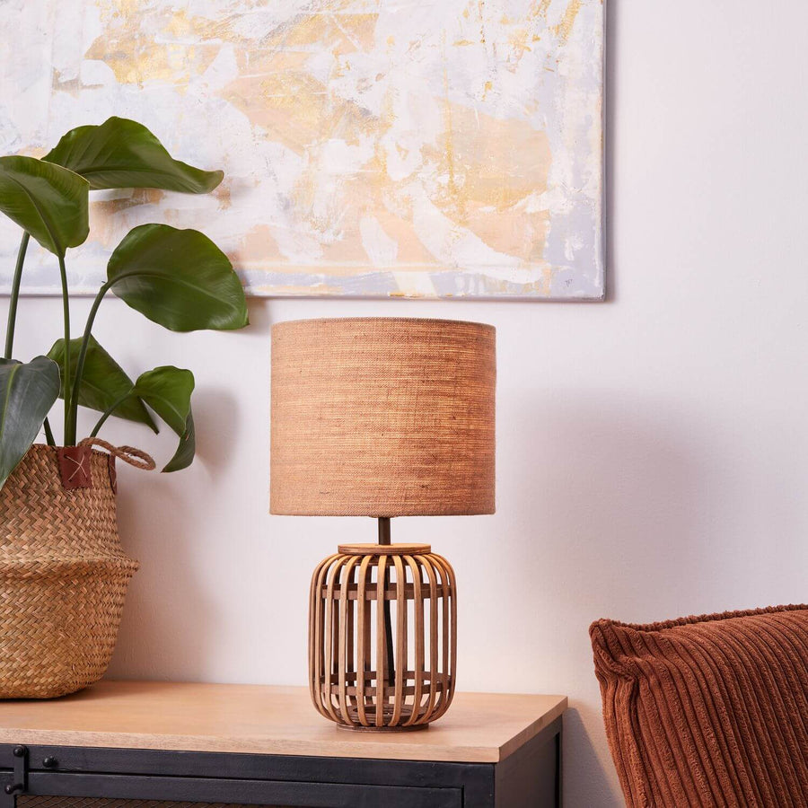 Lampe posée sur un meuble clair, tableau abstrait et plante verte derrière