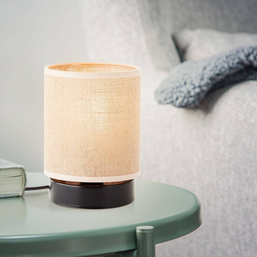 Lampe à poser allumée sur une table basse verte devant un canapé gris flou