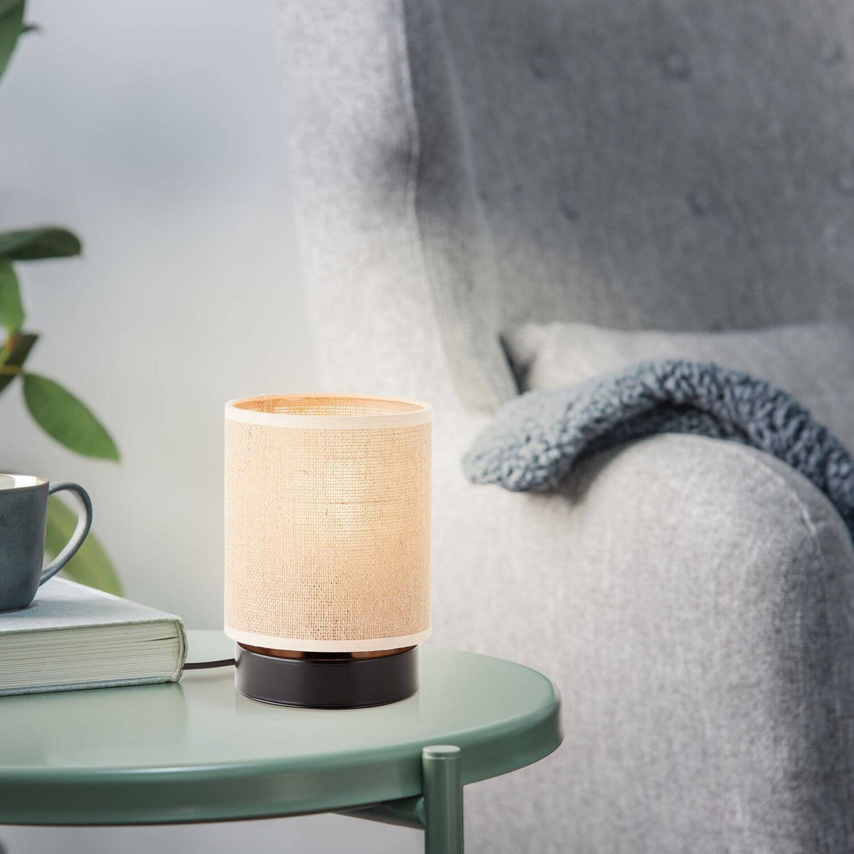 Mise en ambiance avec lampe allumée, tasse, livre et plante sur table verte