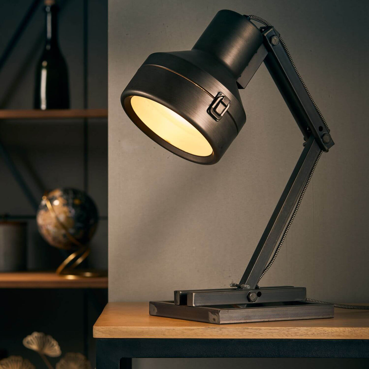 Lampe allumée posée sur table en bois, lumière dorée, décor avec globe et bouteille en arrière-plan.