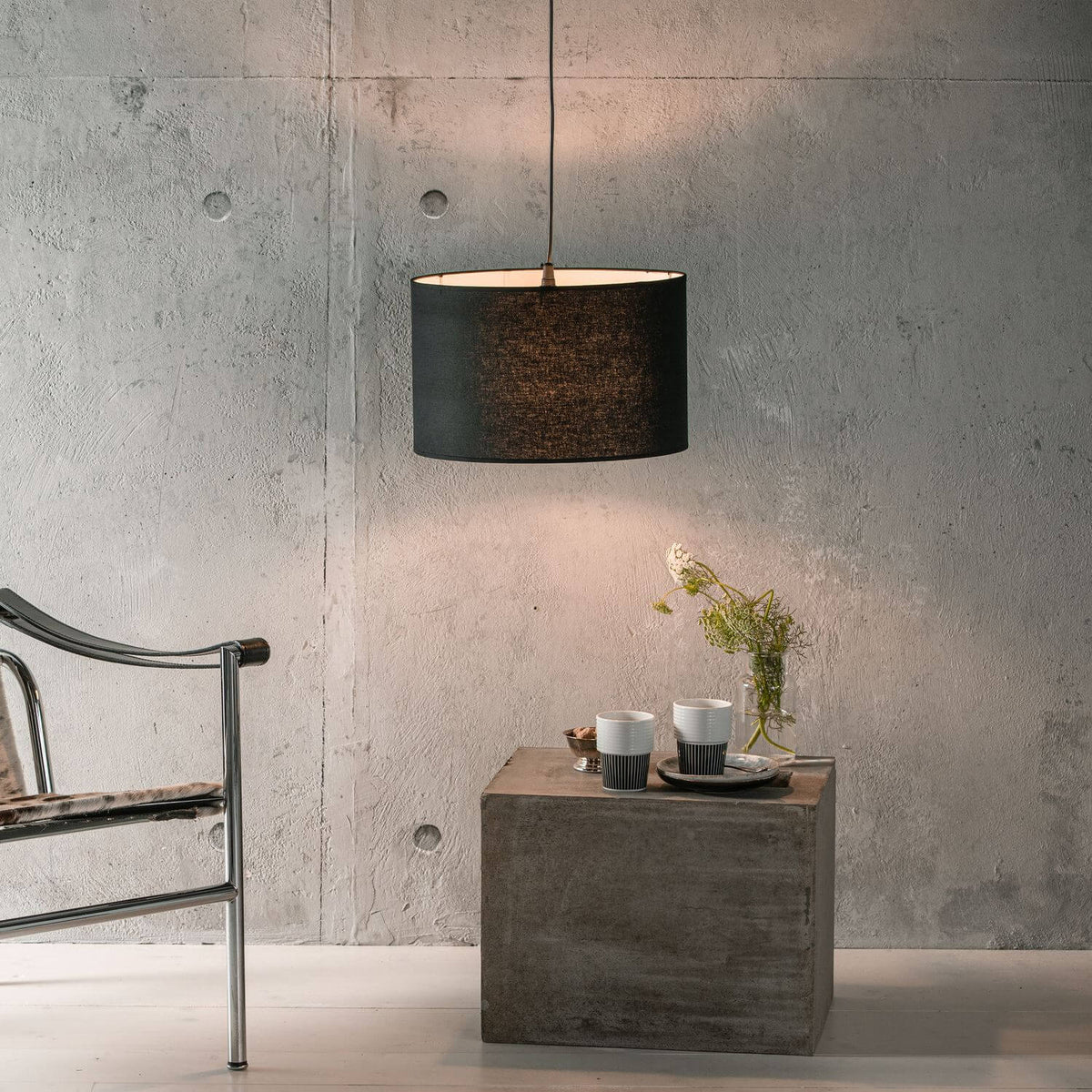 Mise en ambiance du luminaire suspendu au-dessus d'un cube en béton, près d'un fauteuil
